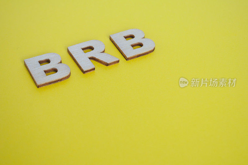 在黄色背景上代表Be Right Back的BRB木制字母